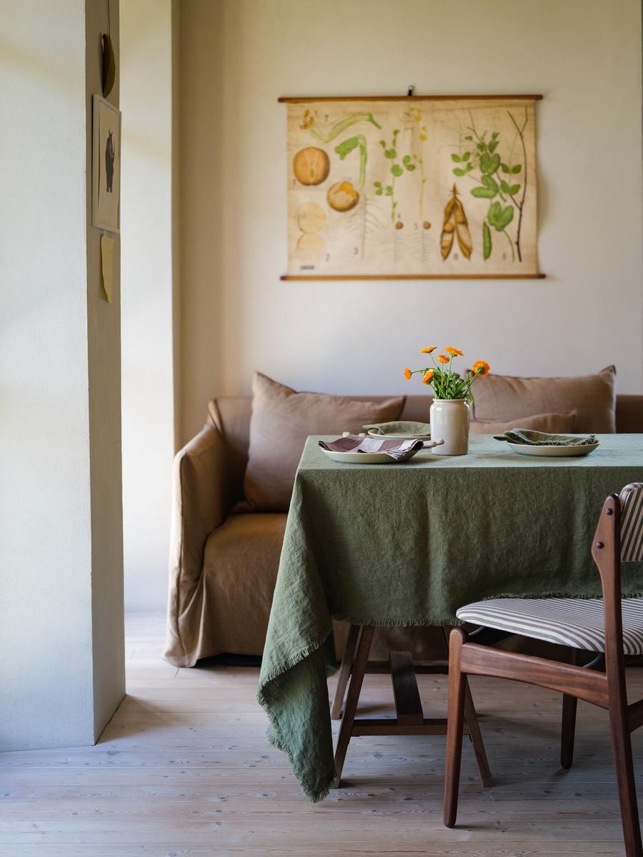 Olivgrüne Terra Fringe Leinentischdecke mit cremefarbenen Tellern und orangefarbenen Blumen