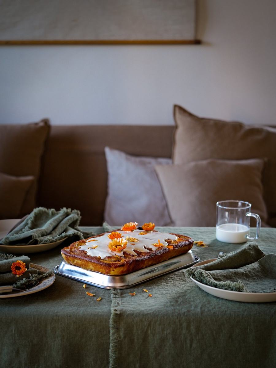 Kuchen mit orangefarbenen Blumen auf olivgrünem Leinen und Fransenservietten