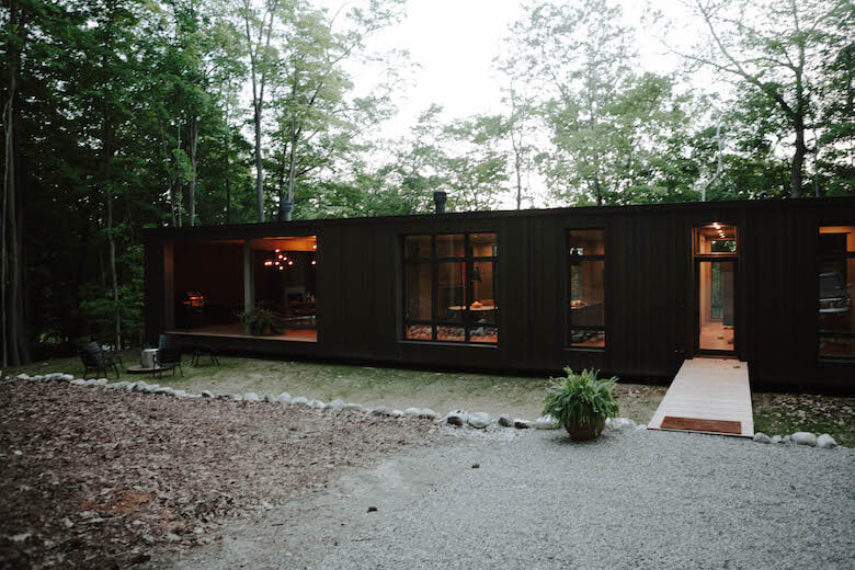 Das beleuchtete Hygge-Supply-Haus Birch Le zwischen Bäumen in der Dämmerung