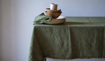 Olivgrüne Terra Fringe Leinentischdecke mit Serviette, cremefarbenen Tellern und Holzschalen